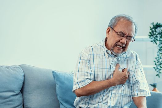 An agonizing senior man suffering from chest pain or heart attack alone in his living room. Serious health problem and feeling unwell concept for seniors.