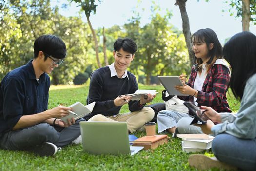 Group of university students reading book on green lawn at university campus. Youth lifestyle, university and friendship concept.