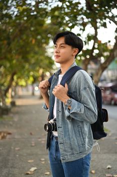 Happy asian man traveller in hipster outfit spending free time outdoors, walking in the city street on beautiful day.