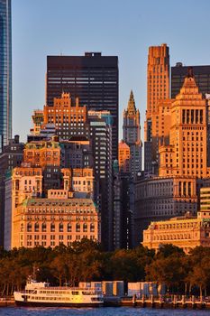Image of Empire State Building through streets of New York City from off of coast in golden glow sunset dusk light