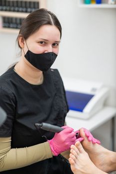 The pedicure master processes the client's foot using an apparatus with an abrasive disc