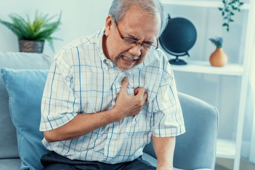 An agonizing senior man suffering from chest pain or heart attack alone in his living room. Serious health problem and feeling unwell concept for seniors.