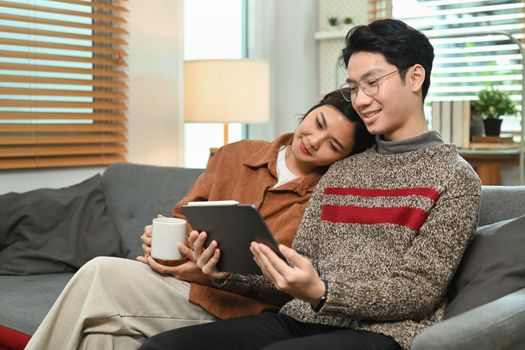 Happy loving young couple watching video, surfing internet on digital tablet while spending time together at home.