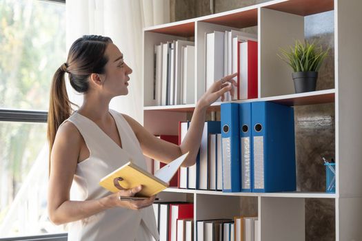 Charming young Asian businesswoman with a smile standing holding documents at the office