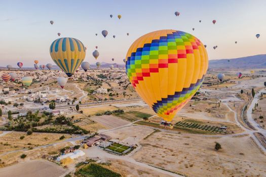 Colorful hot air balloons flying over at fairy chimneys valley in Nevsehir, Goreme, Cappadocia Turkey. Spectacular panoramic drone view of the underground city and ballooning tourism. High quality.