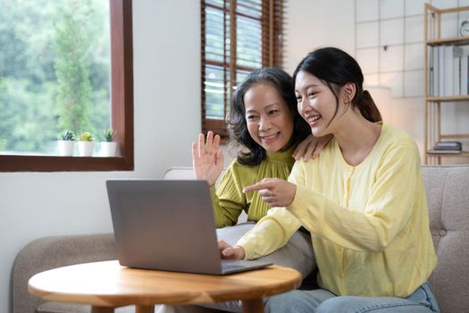 Happy adult granddaughter and senior grandmother having fun enjoying talk sit on sofa in modern living room, smiling old mother hugging young grown daughter bonding chatting relaxing at home together.