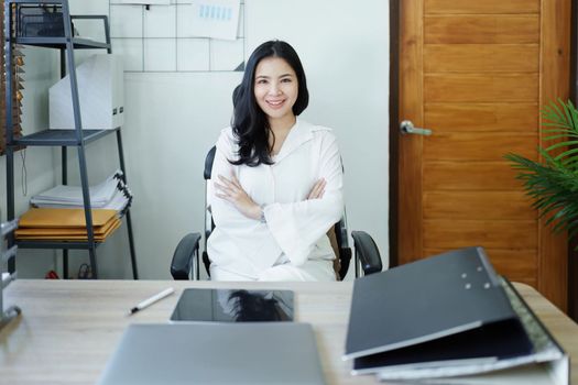 Portrait of a woman business owner showing a happy smiling face as he has successfully invested her business using computers and financial budget documents at work.