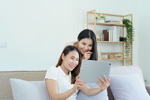 lgbtq, lgbt concept, homosexuality, portrait of two asian women posing happy together and loving each other while playing tablet at sofa.