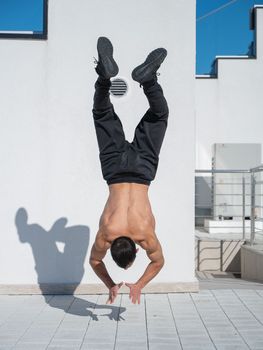 Man doing a handstand outdoors against a white wall