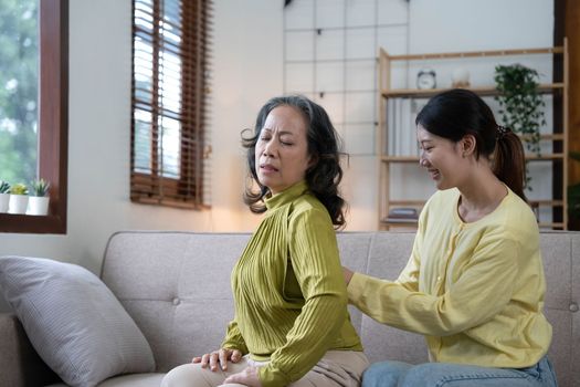 Asian daughter giving an elderly mother a relaxing massage while sitting on the sofa.