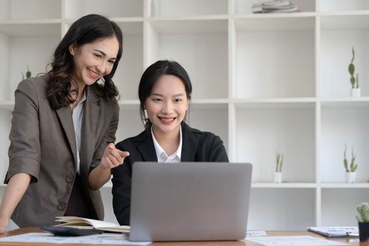 Two young Asian business woman talk, consult, discuss working with new startup project idea presentation analyze plan marketing and investment in the office...