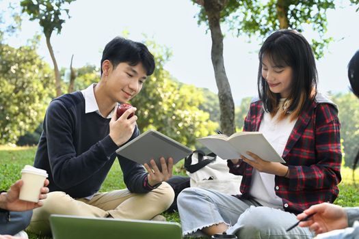 Image of university students chatting with each other after class while sitting on grass in the campus. Education and lifestyle concept.