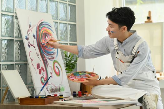 Pleasant man artist creating artwork with watercolor on canvas, enjoy creativity activity at home. Art and leisure activity concept.