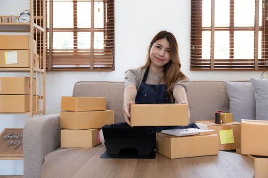 Asian business woman leaning on the sofa use laptop computer checking customer order online shipping boxes at home. Starting Small business entrepreneur SME