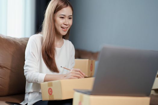 Starting small business entrepreneur of independent young Asian woman online seller is using computer and taking orders to pack products for delivery to customers. SME delivery concept.