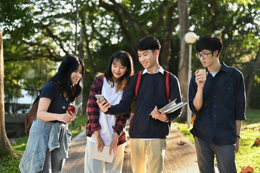 Group of friendly university students are talking to each other after classes while walking in university campus outdoors.