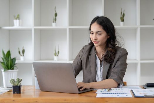 Portrait of serious young businesswoman accountant in formal wear sitting at her work place and use laptop, summarizing taxes, planning future investments, accounting at office...