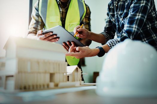 Engineers are consulting the team to design an architectural structure for clients with blueprints and building models to work at office.
