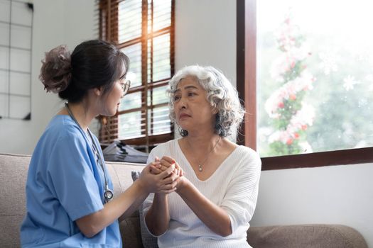 Happy patient is holding caregiver for a hand while spending time together. Elderly woman in nursing home and nurse...