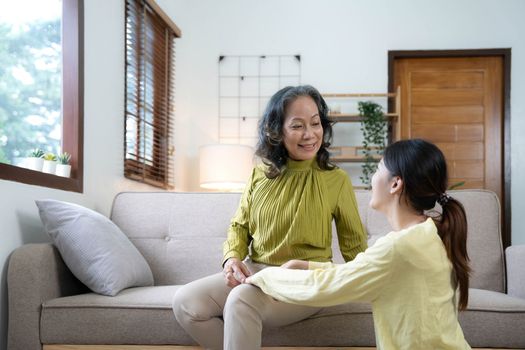 Asian daughter giving an elderly mother a relaxing massage while sitting on the sofa.