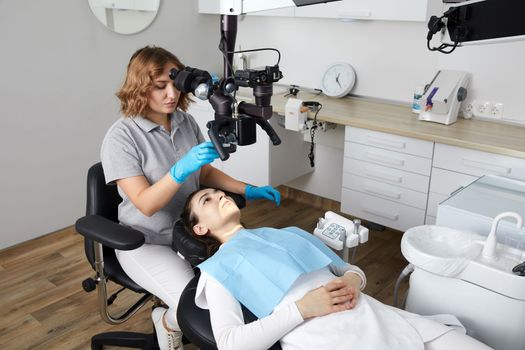 Female dentist with dental tools and microscope treating patient teeth at dental clinic office. Medicine, dentistry and health care concept. Dental equipment