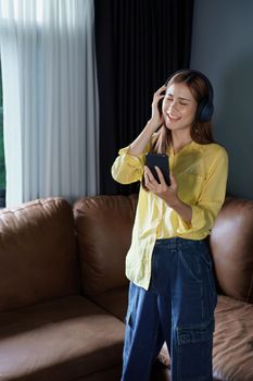 Portrait of asian woman using smart phone mobile and headphones relaxing on sofa at home.