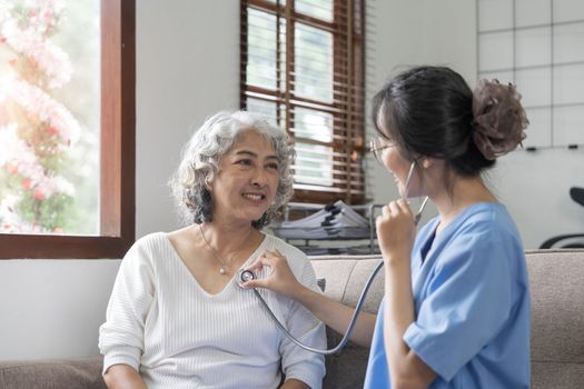 Happy patient is holding caregiver for a hand while spending time together. Elderly woman in nursing home and nurse...