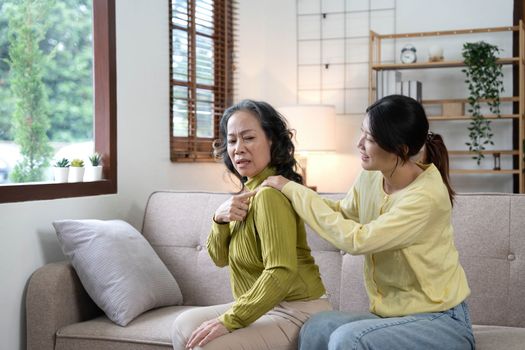 Asian daughter giving an elderly mother a relaxing massage while sitting on the sofa.