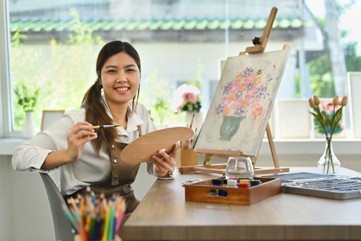 Beautiful young Asian woman enjoying creativity activity, painting in art workshop. Hobby and leisure concept.