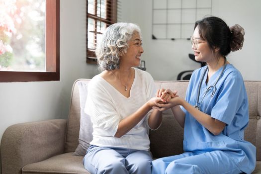 Happy patient is holding caregiver for a hand while spending time together. Elderly woman in nursing home and nurse...