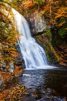 Image of Forest rocky cliffs covered in golden leaves by large blurred waterfall raging