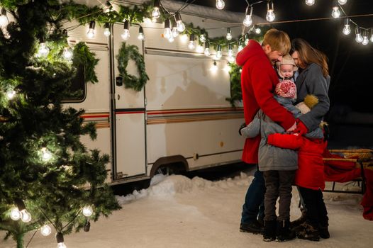 Happy caucasian family hugging outdoors. Christmas decorations. Parents and three sons travel in a camper