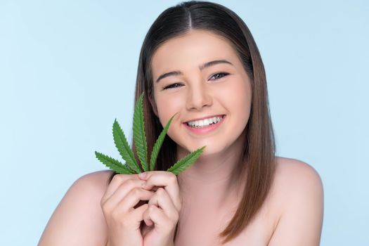 Closeup portrait of charming girl with fresh skin holding green leaf for beauty skin care made from cannabis leaf. Cosmetology and cannabis concept with isolated background.