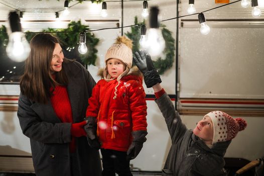 Caucasian woman and two with sons celebrate Christmas in a camper. The mother of two boys decorates the van with Christmas lights