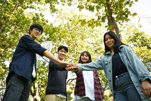 Image of young people celebrating together while stacking hands outdoor. Relationship youth and community concept.