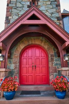 Image of Straight on pair of red arched doors with stone wall and red plants