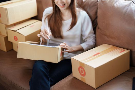 Starting small business entrepreneur of independent young Asian woman online seller is using tablet computer and taking orders to pack products for delivery to customers. SME delivery concept.