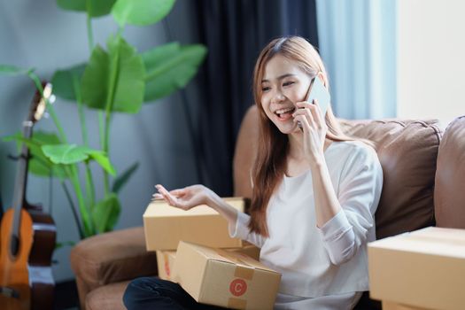 Starting small business entrepreneur of independent Asian female online seller talking on the phone with a customer and packing products for delivery to the customer. and SME delivery concept.