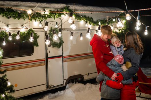 Happy caucasian family hugging outdoors. Christmas decorations. Parents and three sons travel in a camper