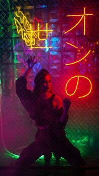Caucasian woman in neon studio behind chain-link mesh