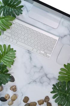 Stylish workplace with computer and green leaf on marble background.