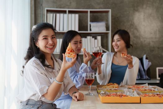 Friends at birthday party clinking glasses with champagne and pizza, enjoying Christmas vacation, pizza on the table. Holiday Party event.