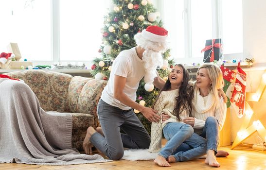 Picture of happy family celebrating New Year eve, little girl with parents enjoying winter holidays, father wearing Santa Claus costume, Christmas magic, happiness and love concept.