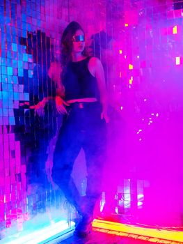 Portrait of a caucasian woman in sunglasses in neon light against a mirror wall