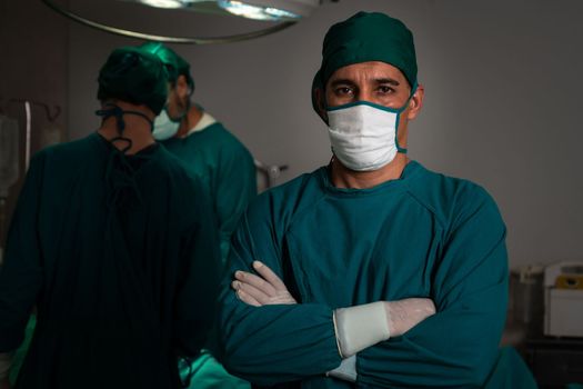 Portrait of surgical team leader in sterile operating room with his team and patient undergoing surgery. Confident and professional surgeon in full protective wear provide medical care to his patient.