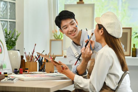 Asian man painting face his girlfriend during painting in at art studio. Leisure activity, creative hobby and art concept.