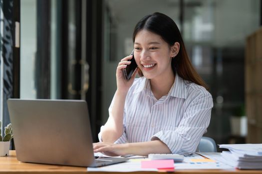 Happy Asian business woman talking with client on the cell phone.