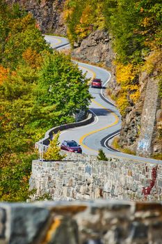 Image of Winding road with cars and stone wall going up through cliffs and forest