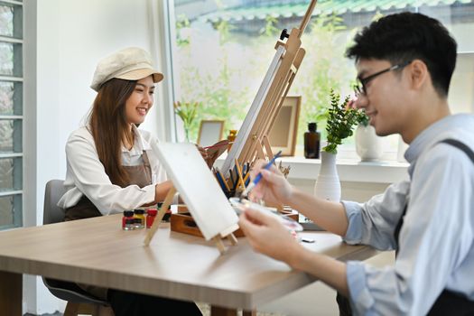 Two young creative people painting picture with watercolor on canvas at art school studio. creativity, education and people concept.