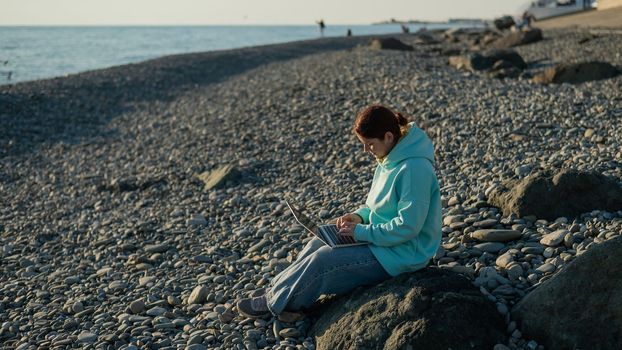 Caucasian woman working freelance on laptop on the beach